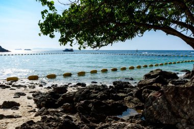 Berrak mavi sularda kayaları olan tropikal bir plajın manzarası ve Koh Larn adasında gün batımında açık bir gökyüzünde dalgalar. Panorama Okyanusu. Pattaya, Tayland, Tekne, Tatil.