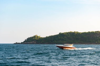 Ada manzarasının arka planında mavi tropikal denizde yüzen sürat teknesi ve Koh Larn adasında açık hava günbatımı. Körfezde sürat teknesi, Panorama Okyanusu, Tayland, Tatil.