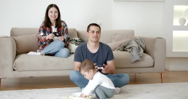 若い家族は家にいる 両親はビデオゲームをしてる女の子は部屋にいる — ストック動画