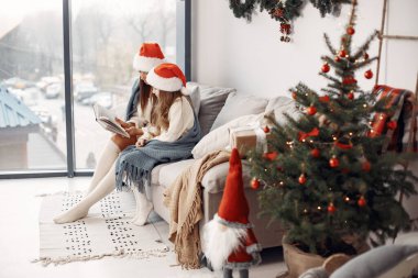 İnsanlar Noel için hazırlanıyor. Anne kızıyla oynuyor. Noel Baba şapkalı bir aile. Beyaz elbiseli küçük kız.