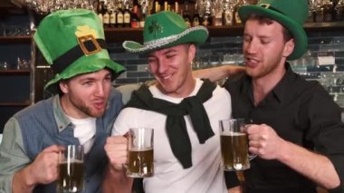 Friends celebrating Saint Patricks Day in a pub, smiling happy man looks at camera and toasts with a mug of beer. Portrait.