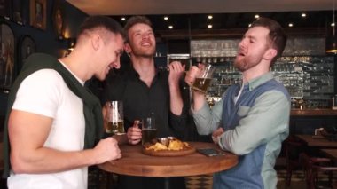 Friends celebrating Saint Patricks Day in a pub, smiling happy man looks at camera and toasts with a mug of beer. Portrait.