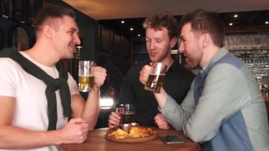 Friends celebrating Saint Patricks Day in a pub, smiling happy man looks at camera and toasts with a mug of beer. Portrait.
