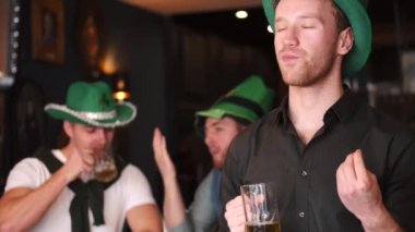 Friends celebrating Saint Patricks Day in a pub, smiling happy man looks at camera and toasts with a mug of beer. Portrait.