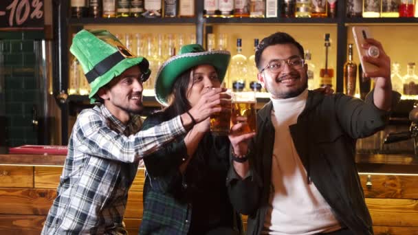 若者の会社は聖パトリックの日を祝う 彼らはバーで楽しんでいます 彼らはカーニバルのヘッドギアに身を包んだ — ストック動画