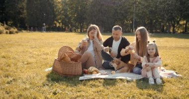 Mutlu aile sonbahar ormanında pikniğin tadını çıkarıyor. İki tatlı kızı ve evcil hayvanı olan beyaz bir aile..