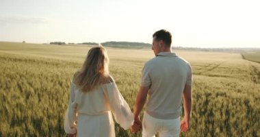 A pregnant woman in a beautiful long dress walks through the field with her husband in a wheat field at sunset. Future parents.
