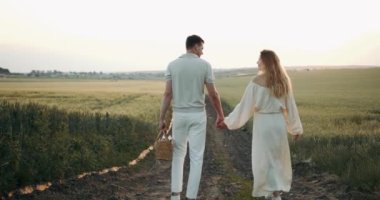 A pregnant woman in a beautiful long dress walks through the field with her husband in a wheat field at sunset. Future parents.