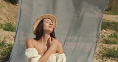 Bozkırda bohem tarzında bir kız. Çayırda şapkalı esmer kız. Kavramsal fotoşoplama. Kumaş fotoğraf alanı.