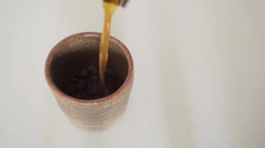 El yapımı zarafet: El yapımı porselen kupaya kahve dökmek. Bir el, porselen bir fincana zengin, aromatik bir kahve döker, ardından da zarif bir bardak kaldırır.