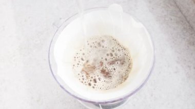 60 Kahve Dökümü: Bir Buharlı Aroma Senfonisi. Elleri kahvenin üzerine kaynar su döküyor, V60 'ı dolduruyor ve buhar sahneyi sararken büyüleyici bir sis yaratıyor.