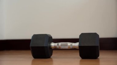 Ev Sağlığı Programı: Bir Dumbbell Kapmak. Eller ahşap zeminde dinlenen bir dambıl için uzanır, ev antrenmanına odaklanarak güç antrenmanına odaklanır.