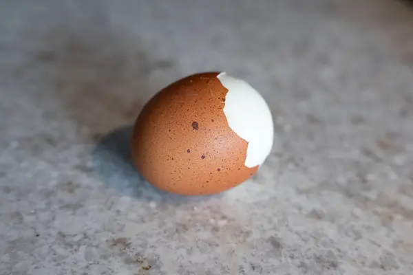 stock image Boiled Egg with Partially Removed Speckled Shell, Revealing White Surface. A boiled egg sits isolated with its speckled shell partially peeled away, revealing a glimpse of the smooth, white egg inside