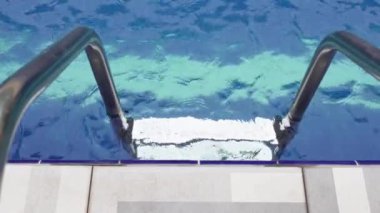 Havuzda metal bir merdiven. Arka planda mavi sularda dalgalanmalar var. Yazın özünü yakalıyor, yüzüyor ve rahatlıyor. Yüzme ve tatil titreşimlerini göstermek için mükemmel.