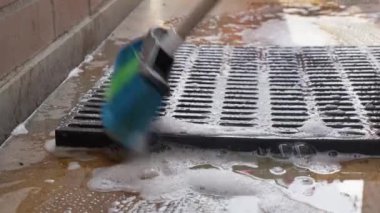 Mavi ve yeşil bir fırça aktif olarak siyah plastik bir paleti sabunlu suyla ovuyor.