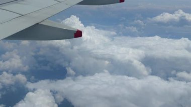 Aşağıdaki kanat ve kabarık beyaz bulutları gösteren bir uçak penceresinden seyahat ve maceranın özünü yansıtan bir manzara.