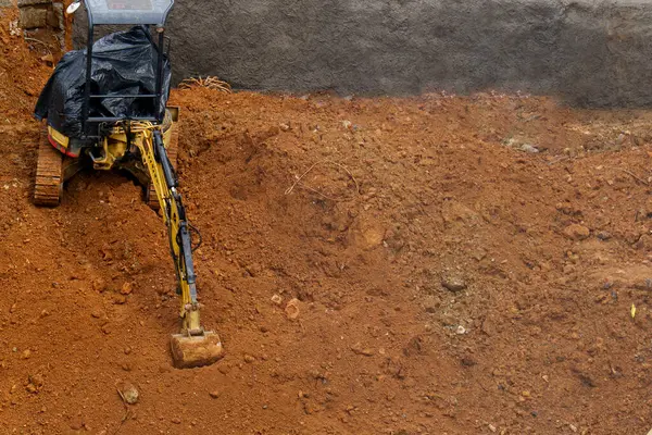 Sarı bir kazıcı, bir inşaat sahasındaki kırmızımsı bir toprak yığınına park etmiş ve geniş bir kopya alanı sunuyor.