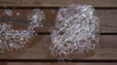 Şeffaf sabun köpükleri kümeler oluşturuyor ve ahşap bir güvertede sönüyor.