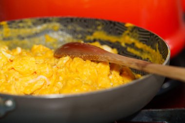 Çırpılmış yumurta, çırpılmamış tavada, tahta kaşıkla pişiriliyor.