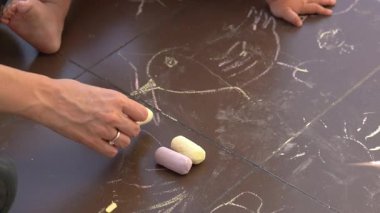 Anne ve çocuk güneşli bir günde kahverengi seramik fayanslara renkli tebeşirle çiziyorlar.