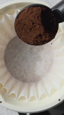 Kahve siyah bir kepçeden kahve filtresine dökülüyor, demlenmeye hazır.