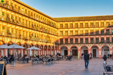 Cordoba, İspanya 18 Aralık 2023: İnsanlar Endülüs 'ün Cordoba kentindeki tarihi bir meydan olan Plaza de la Corredera' da güneşli bir günün tadını çıkarıyorlar. Olay mahalli sakinleri ve ziyaretçileri açık kafelerde otururken yakalıyor.