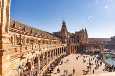 Seville, İspanya 17 Aralık 2023: Ziyaretçiler açık mavi gökyüzüyle güneşli bir günde Plaza de Espana 'da geziniyorlar. Bu sembolik simge, 1929 'daki İbero-Amerikan Sergisi için inşa edildi.