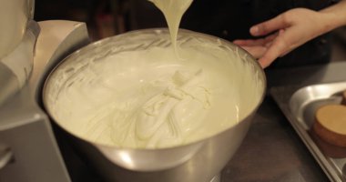 Kremanın tutarlılığını kontrol eden bir şekerlemecinin elinde büyük bir çırpıcı. Krema hazırlanıyor. Kremalı, çırpmalı, aşçı eli olan bir kâseye yaklaş..