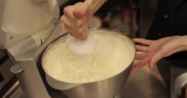 Kremanın tutarlılığını kontrol eden bir şekerlemecinin elinde büyük bir çırpıcı. Krema hazırlanıyor. Kremalı, çırpmalı, aşçı eli olan bir kâseye yaklaş..