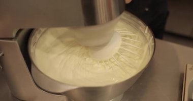 Kremanın tutarlılığını kontrol eden bir şekerlemecinin elinde büyük bir çırpıcı. Krema hazırlanıyor. Kremalı, çırpmalı, aşçı eli olan bir kâseye yaklaş..