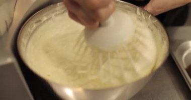 Kremanın tutarlılığını kontrol eden bir şekerlemecinin elinde büyük bir çırpıcı. Krema hazırlanıyor. Kremalı, çırpmalı, aşçı eli olan bir kâseye yaklaş..