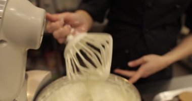 Kremanın tutarlılığını kontrol eden bir şekerlemecinin elinde büyük bir çırpıcı. Krema hazırlanıyor. Kremalı, çırpmalı, aşçı eli olan bir kâseye yaklaş..