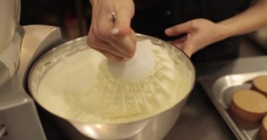 Kremanın tutarlılığını kontrol eden bir şekerlemecinin elinde büyük bir çırpıcı. Krema hazırlanıyor. Kremalı, çırpmalı, aşçı eli olan bir kâseye yaklaş..