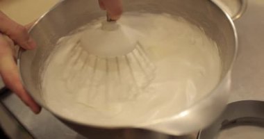 Kremanın tutarlılığını kontrol eden bir şekerlemecinin elinde büyük bir çırpıcı. Krema hazırlanıyor. Kremalı, çırpmalı, aşçı eli olan bir kâseye yaklaş..