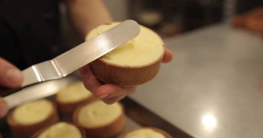 Kremalı tart hazırlamak için. Kremayı yaydığı sırada hamur işi şefinin elinde mini bir tart. Pasta şefi tartı beyaz kremayla süslüyor.