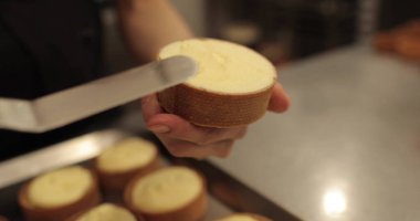 Kremalı tart hazırlamak için. Kremayı yaydığı sırada hamur işi şefinin elinde mini bir tart. Pasta şefi tartı beyaz kremayla süslüyor.