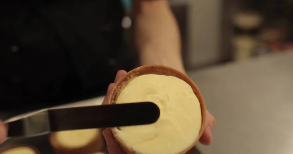 Kremalı tart hazırlamak için. Kremayı yaydığı sırada hamur işi şefinin elinde mini bir tart. Pasta şefi tartı beyaz kremayla süslüyor.
