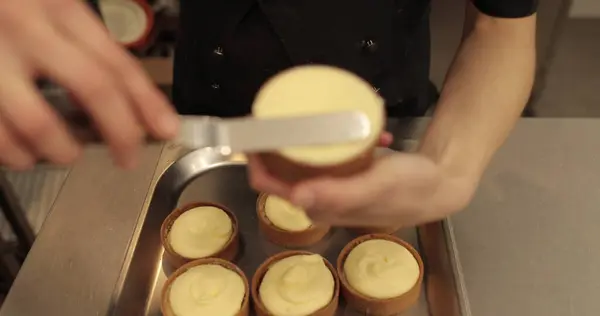 Kremalı tart hazırlamak için. Kremayı yaydığı sırada hamur işi şefinin elinde mini bir tart. Pasta şefi tartı beyaz kremayla süslüyor.