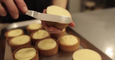 Kremalı tart hazırlamak için. Kremayı yaydığı sırada hamur işi şefinin elinde mini bir tart. Pasta şefi tartı beyaz kremayla süslüyor.