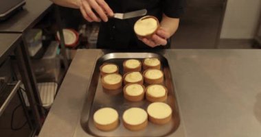 Kremalı tart hazırlamak için. Kremayı yaydığı sırada hamur işi şefinin elinde mini bir tart. Pasta şefi tartı beyaz kremayla süslüyor.