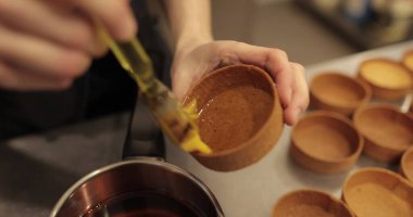 Şekerlemecinin ellerine yakın plan fırçayla tart sürerken. Profesyonel bir pastacı tarafından tartların hazırlanması.