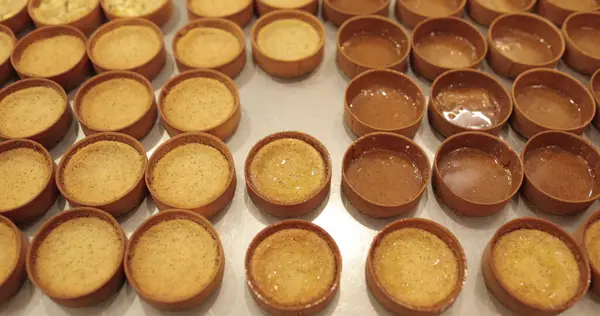 Çok sayıda mini tart, bir hamur fırçası yardımıyla onları elma şurubuyla hamile bırakma sürecinde profesyonel bir hamur işi masasına dizilir..