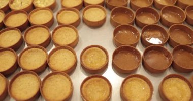 Çok sayıda mini tart, bir hamur fırçası yardımıyla onları elma şurubuyla hamile bırakma sürecinde profesyonel bir hamur işi masasına dizilir..