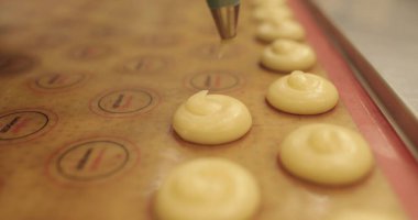 Pişirme tepsisinin yüzeyine krem sıkan bir yemek şırıngasının yakın çekimi. Pişirme şırıngası kullanarak kek pişirmek