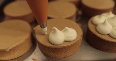 Aşçılık şırıngası kullanarak tartlara krema süslemek. Profesyonel şekerleme mutfağı. Profesyonel bir şekerci tarafından tartların toplu dekorasyonu.