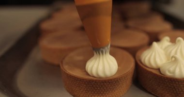 Aşçılık şırıngası kullanarak tartlara krema süslemek. Profesyonel şekerleme mutfağı. Profesyonel bir şekerci tarafından tartların toplu dekorasyonu.