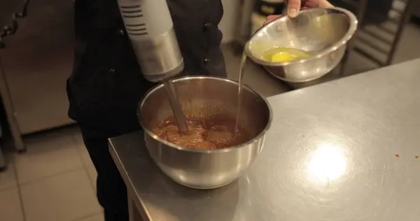 Dalış blenderi çalışırken yumurtaları kaseye ekliyorum. Profesyonel bir mutfakta hamur işi hazırlama.