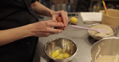 Bir kadının yumurtalarını kırdığı ve profesyonel bir mutfakta hamur yaptığı için kaseye eklediği yakın plan..