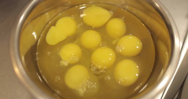 Çiğ tavuk yumurtaları, profesyonel bir pasta mutfağının masasında metal bir kaseye kırılır..
