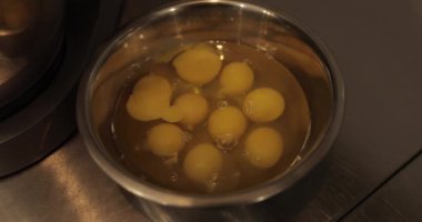 Çiğ tavuk yumurtaları, profesyonel bir pasta mutfağının masasında metal bir kaseye kırılır..